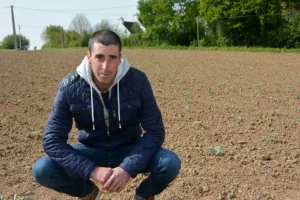 Un producteur de légumes finistérien accroupi dans un champ.