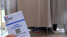 Carte électorale tenue en main devant des isoloirs