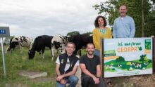 Des éleveurs près d'un panneau de ferme devant des vaches au pâturage.