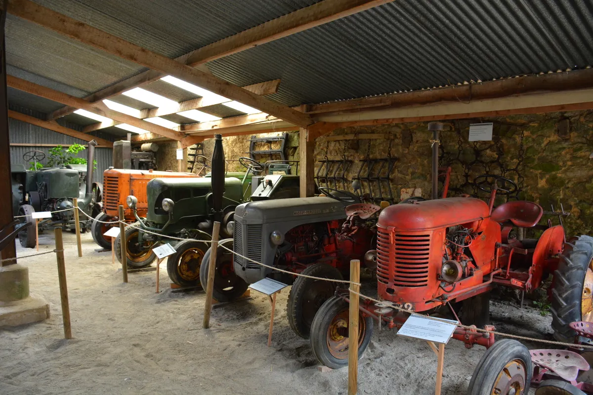 Des vieux tracteurs et du matériel agricole sont exposés sous un hangar de la ferme d'antan