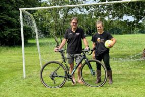 Un éleveur avec son vélo accompagné par sa salariée tenant un ballon de football.