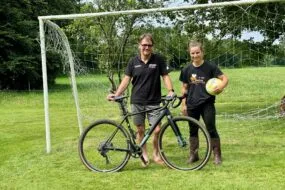 Un éleveur avec son vélo accompagné par sa salariée tenant un ballon de football.