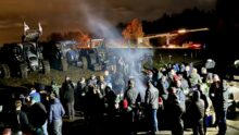 Des agriculteurs manifestant au bord d'un rond-point où sont garés des tracteurs.
