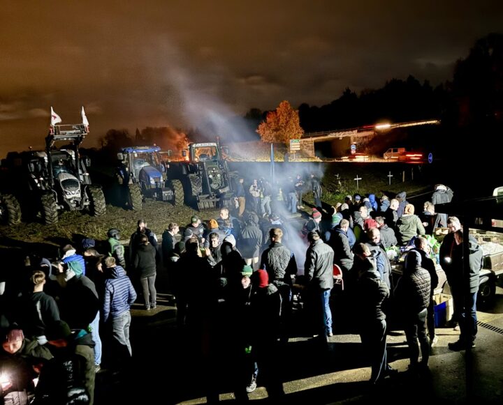 Des agriculteurs manifestant au bord d'un rond-point où sont garés des tracteurs.