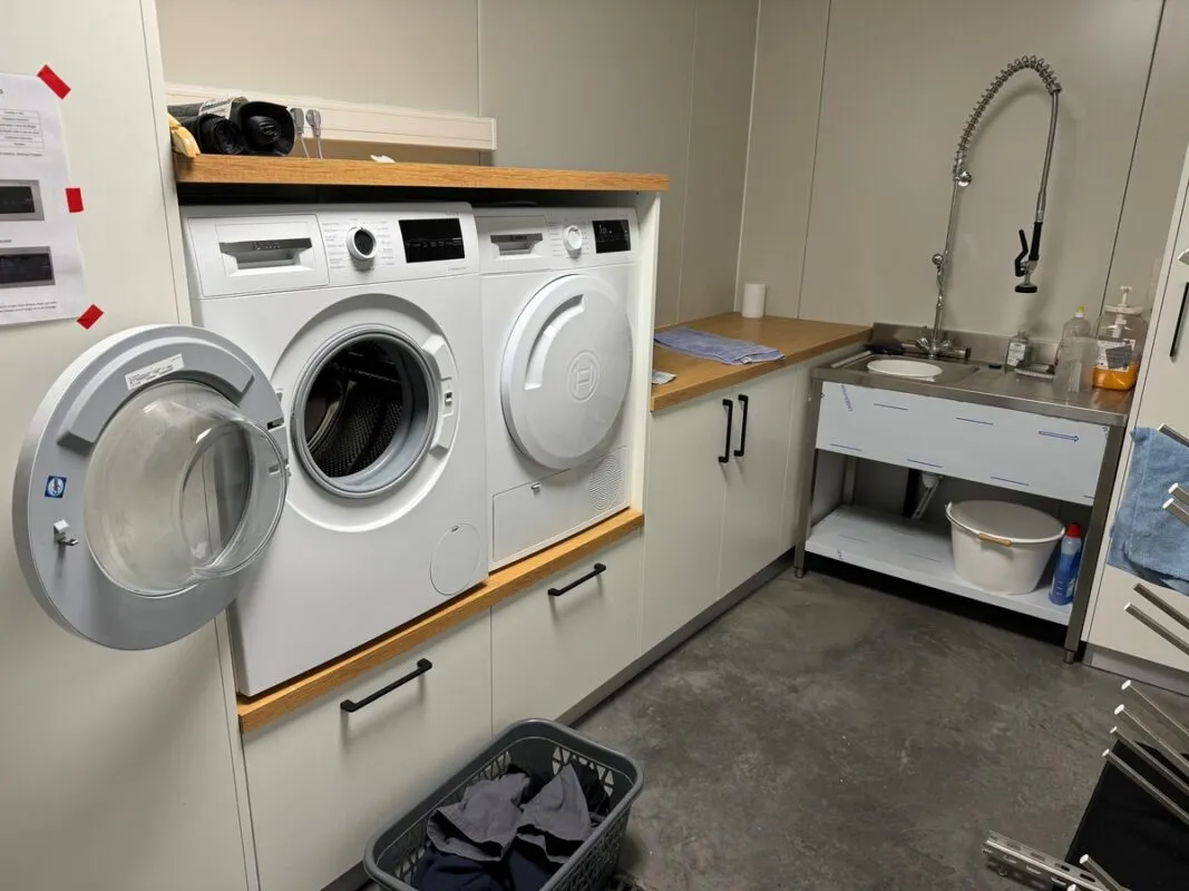 Une pièce équipée d’une machine à laver, d’un sèche-linge et d’un évier avec douchette.