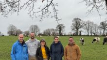 Trois hommes et deux femmes devant un eprairie avec des vaches laitières au pâturage