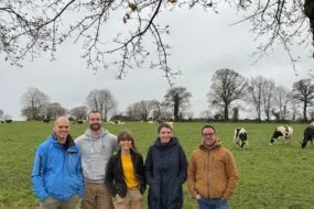 Trois hommes et deux femmes devant un eprairie avec des vaches laitières au pâturage