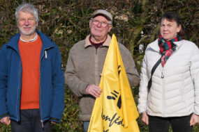 Deux hommes et une femme retraités avec un drapeau jaune du syndicat agricole de la Confédération paysanne
