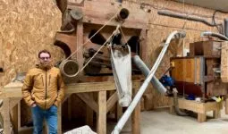 Un paysan pastier devant deux machines anciennes en bois permettant de travailler le grain.