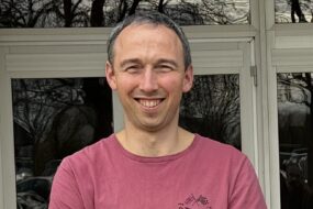 un homme souriant les bras croisés devant un bâtiment