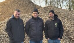 Trois hommes devant un tas de bois déchiqueté.