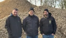 Trois hommes devant un tas de bois déchiqueté.