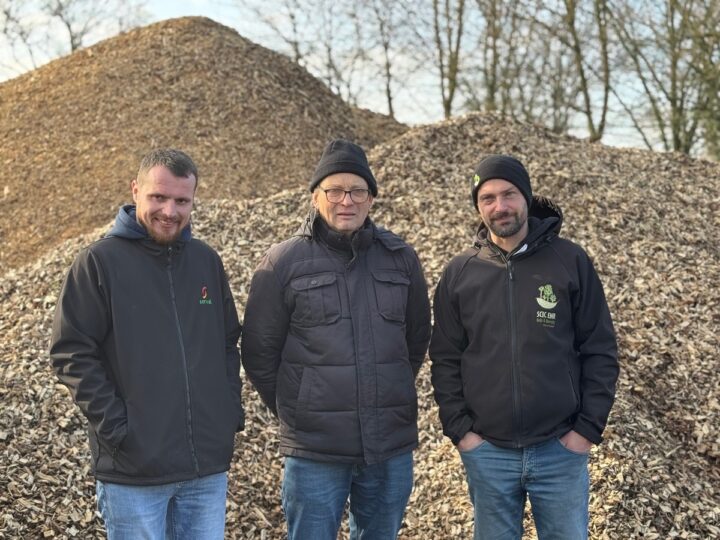 Trois hommes devant un tas de bois déchiqueté.