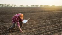 un homme baissé dans un champ labouré avec un ordinateur à la main