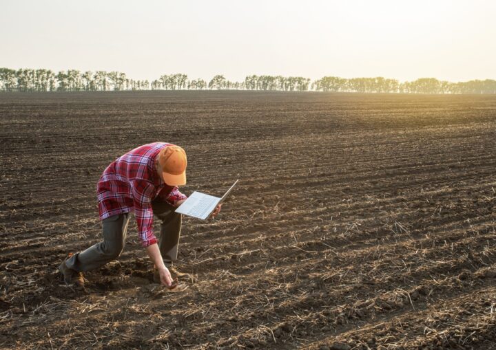 un homme baissé dans un champ labouré avec un ordinateur à la main