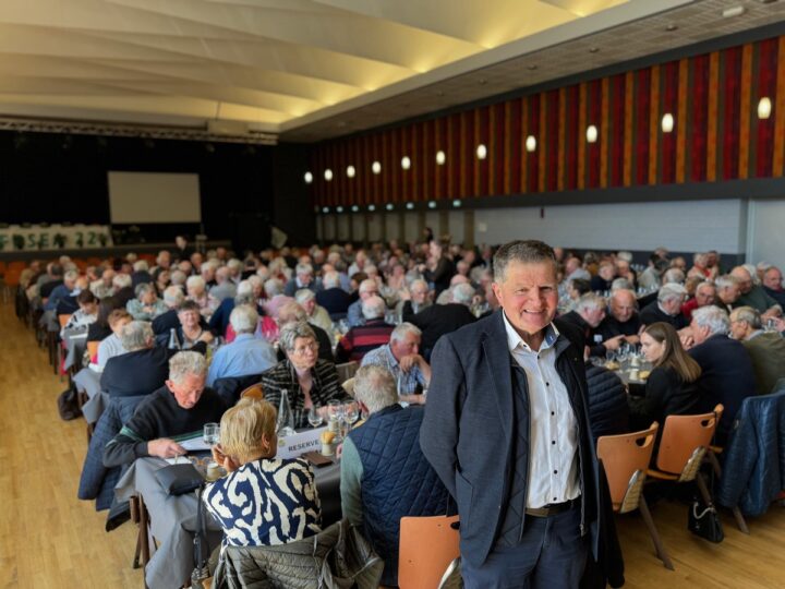 Un homme souriant devant une assemblée de personnes assises.