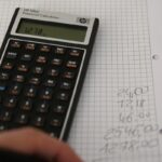 Un main, un cahier et une calculatrice. La main reporte les résultats des calculs sur le cahier