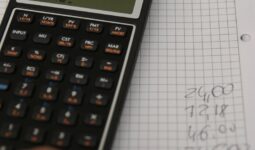Un main, un cahier et une calculatrice. La main reporte les résultats des calculs sur le cahier