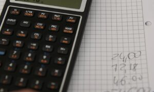 Un main, un cahier et une calculatrice. La main reporte les résultats des calculs sur le cahier