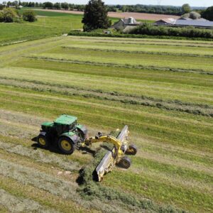 Vue aérienne d'un tracteur au champ avec un andaineur à tapis