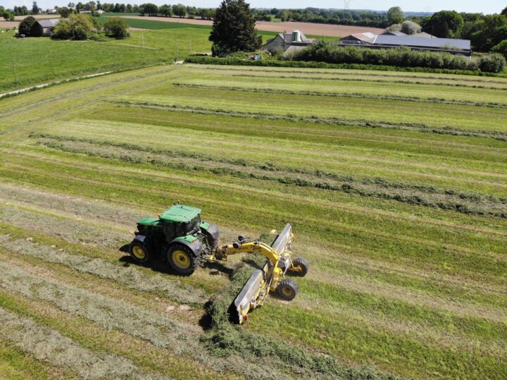 Vue aérienne d'un tracteur au champ avec un andaineur à tapis
