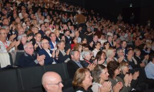 Une foule dans un amphithéâtre assise sur des fauteuils