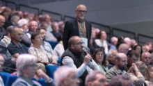Une assemblée sur des gradins, un homme tient un micro