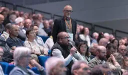 Une assemblée sur des gradins, un homme tient un micro