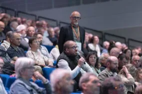 Une assemblée sur des gradins, un homme tient un micro