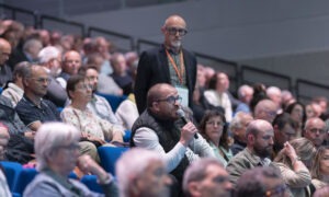 Une assemblée sur des gradins, un homme tient un micro