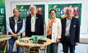 Les responsables du space derrière une table et devant les panneaux de l'affiche 2025