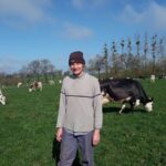 Un éleveur portant un bonnet devant un troupeau de vaches en train de brouter.