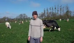 Un éleveur portant un bonnet devant un troupeau de vaches en train de brouter.