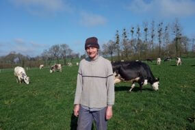 Un éleveur portant un bonnet devant un troupeau de vaches en train de brouter.