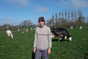 Un éleveur portant un bonnet devant un troupeau de vaches en train de brouter.