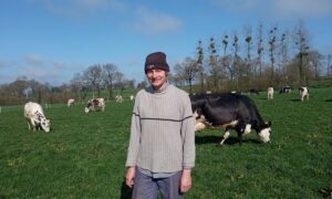 Un éleveur portant un bonnet devant un troupeau de vaches en train de brouter.