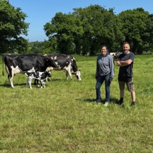 Une femme et un homme dans une prairie avec des vaches Holstein et un veau.