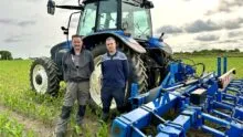 Deux personnes devant un tracteur dans un champ de maïs.