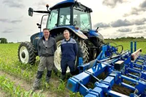 Deux personnes devant un tracteur dans un champ de maïs.