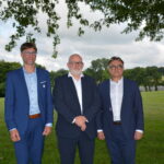 Trois hommes en costume prennent la pose sous un arbre avec un paysage bocager en arrière plan