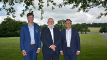 Trois hommes en costume prennent la pose sous un arbre avec un paysage bocager en arrière plan