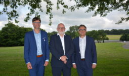 Trois hommes en costume prennent la pose sous un arbre avec un paysage bocager en arrière plan