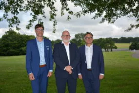 Trois hommes en costume prennent la pose sous un arbre avec un paysage bocager en arrière plan
