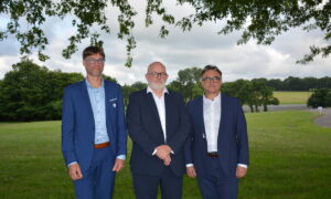 Trois hommes en costume prennent la pose sous un arbre avec un paysage bocager en arrière plan