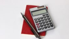 Un carnet, un crayon et une calculatrice posés sur une table blanche