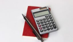 Un carnet, un crayon et une calculatrice posés sur une table blanche