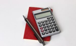 Un carnet, un crayon et une calculatrice posés sur une table blanche