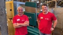 Deux hommes avec un T-shirt rouge devant un robot de traite vert.