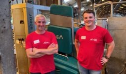 Deux hommes avec un T-shirt rouge devant un robot de traite vert.