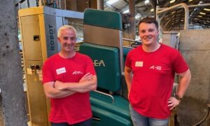 Deux hommes avec un T-shirt rouge devant un robot de traite vert.